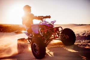 Competitive quad biker with bright sun flare behind driving in a desert race